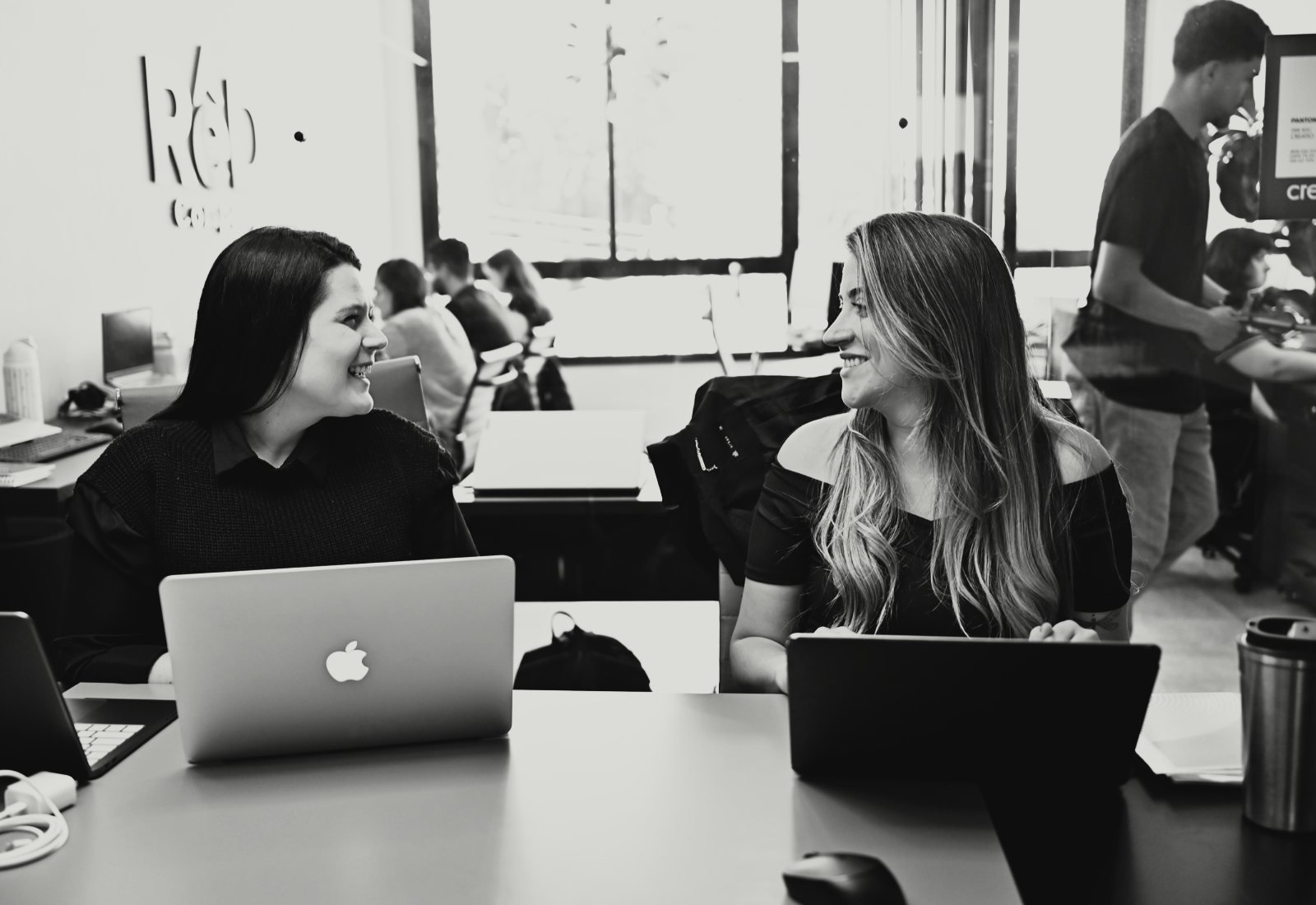 Duas integrantes da equipe da Creatio conversando durante o trabalho, cada uma com seu notebook.